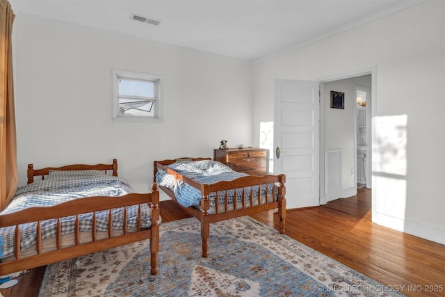 bedroom with baseboards, crown molding, visible vents, and wood finished floors