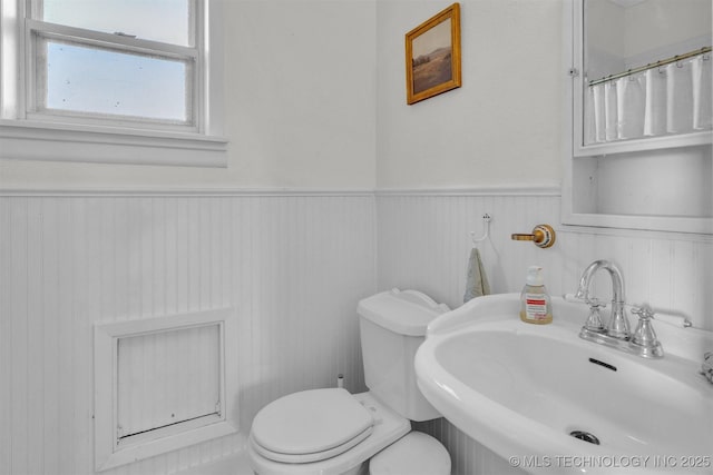 full bathroom featuring toilet, a sink, and wainscoting