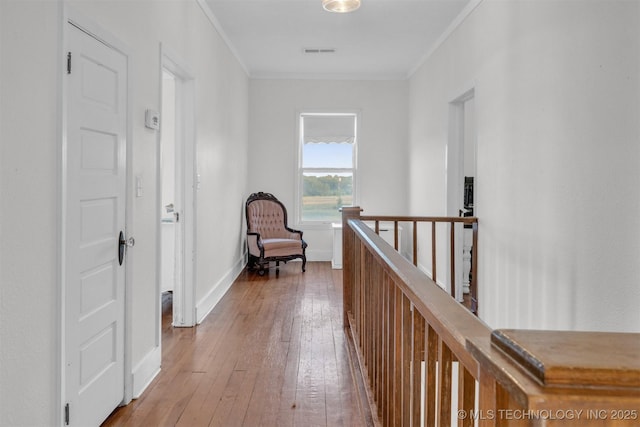 corridor with visible vents, baseboards, an upstairs landing, wood-type flooring, and crown molding