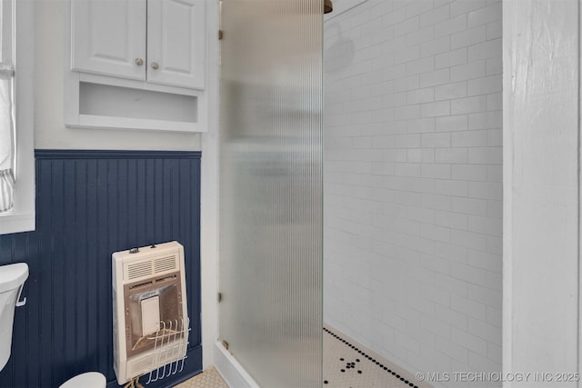 full bath with heating unit, toilet, tiled shower, and wainscoting