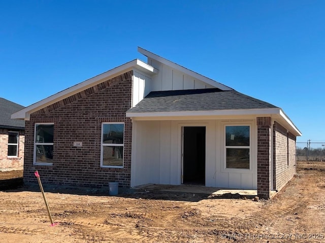 back of house featuring brick siding, board and batten siding, and a shingled roof