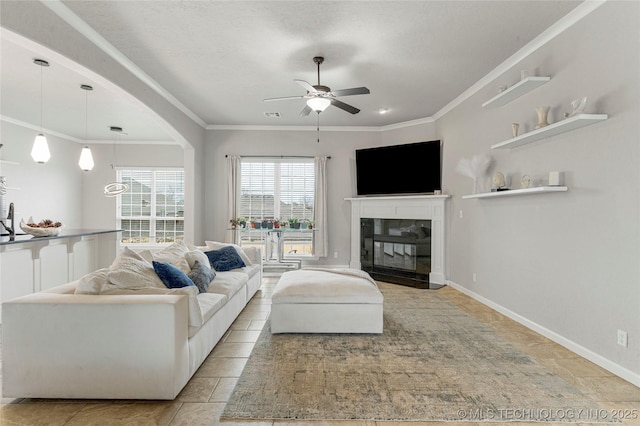 living area with a glass covered fireplace, crown molding, baseboards, and ceiling fan