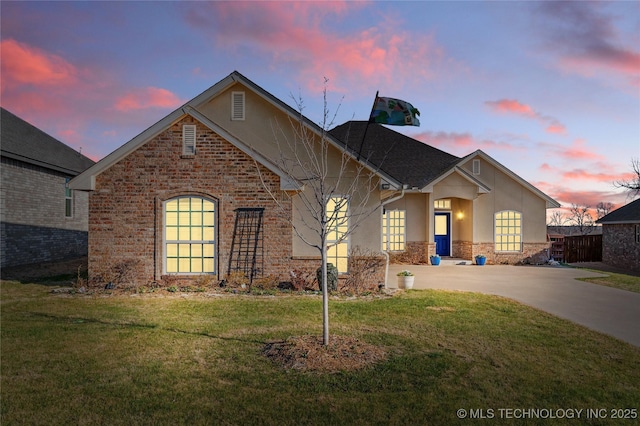 view of front facade with driveway, brick siding, fence, a yard, and stucco siding