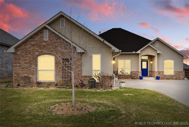 view of front of home with brick siding, stucco siding, concrete driveway, and a yard