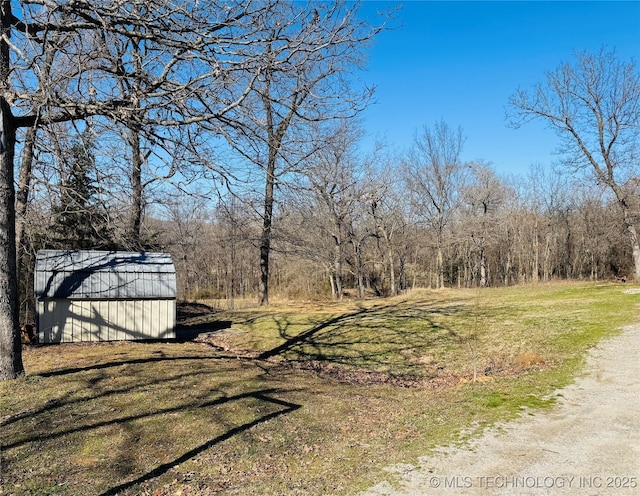 view of yard featuring a storage shed, an outdoor structure, a wooded view, and dirt driveway