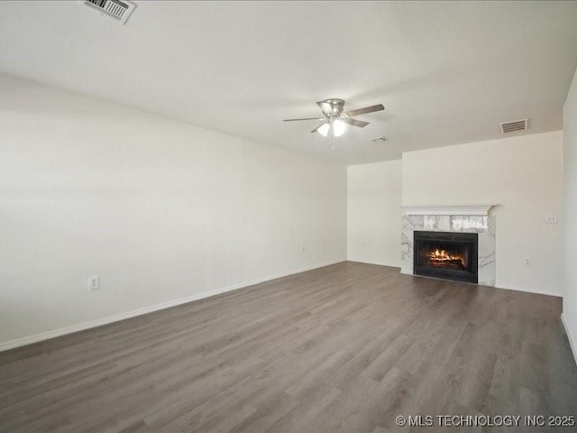 unfurnished living room with ceiling fan, a premium fireplace, wood finished floors, and visible vents