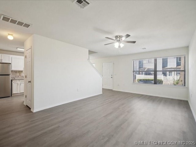 unfurnished living room with a ceiling fan, wood finished floors, visible vents, and baseboards