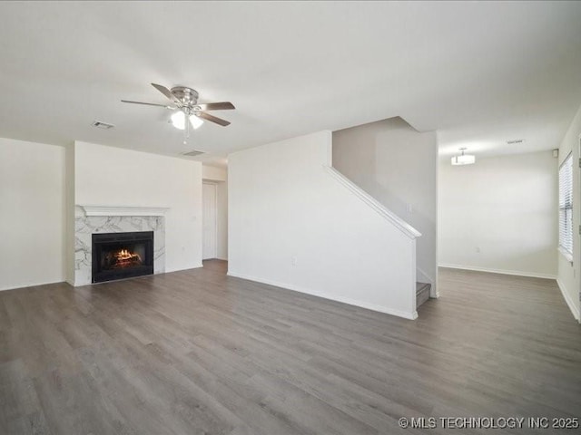 unfurnished living room with wood finished floors, visible vents, a high end fireplace, stairs, and a ceiling fan