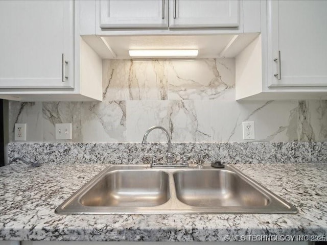 details featuring light stone countertops, backsplash, white cabinets, and a sink