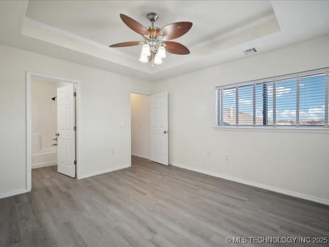 unfurnished bedroom featuring ornamental molding, a tray ceiling, baseboards, and wood finished floors