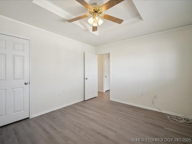 unfurnished room featuring a tray ceiling, crown molding, a ceiling fan, wood finished floors, and baseboards