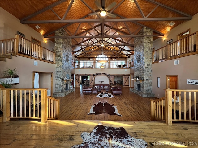 living area with a stone fireplace, beamed ceiling, wooden ceiling, and hardwood / wood-style floors