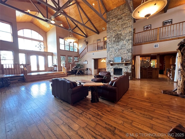 living room with beamed ceiling, a stone fireplace, hardwood / wood-style flooring, and wood ceiling