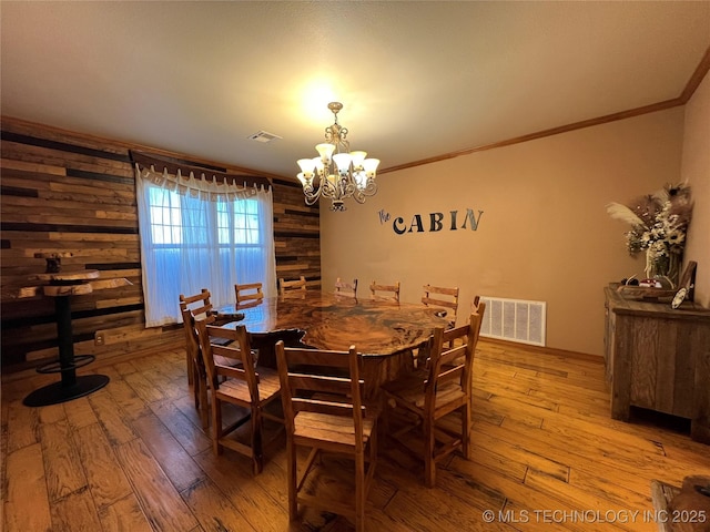 dining room featuring a notable chandelier, wood-type flooring, visible vents, and crown molding