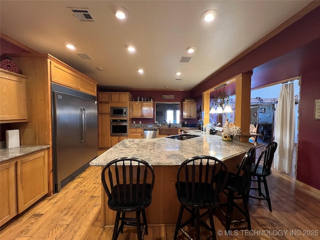 kitchen with built in appliances, a kitchen bar, visible vents, and light wood-style floors