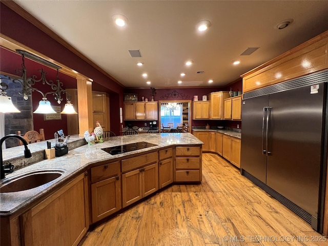 kitchen with black electric stovetop, a sink, light stone countertops, light wood finished floors, and stainless steel built in refrigerator