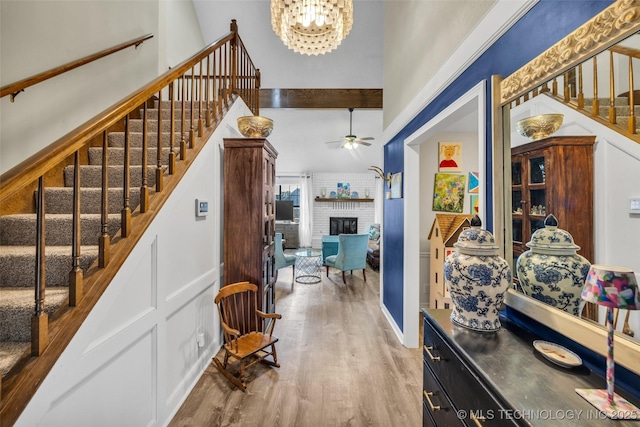 entryway featuring ceiling fan with notable chandelier, a high ceiling, wood finished floors, stairway, and a brick fireplace