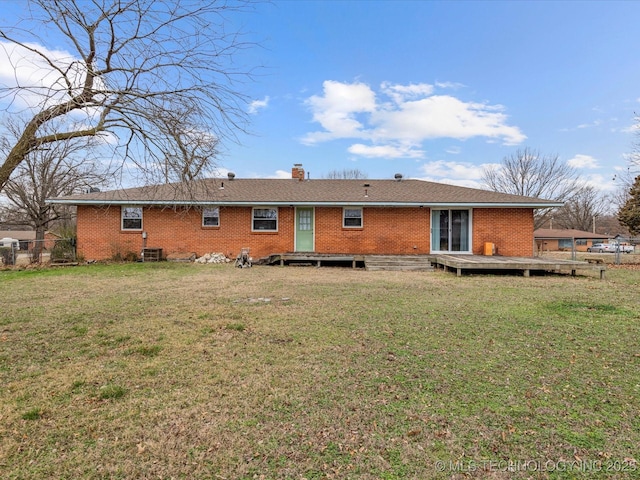 back of house featuring a lawn, a chimney, fence, a wooden deck, and brick siding