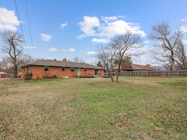 back of property with a chimney, fence, a lawn, and brick siding