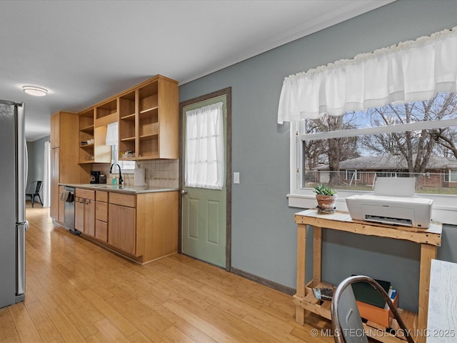 kitchen with light wood finished floors, open shelves, light countertops, appliances with stainless steel finishes, and a sink