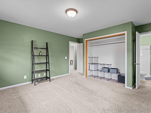 carpeted bedroom featuring a closet, ensuite bath, and baseboards