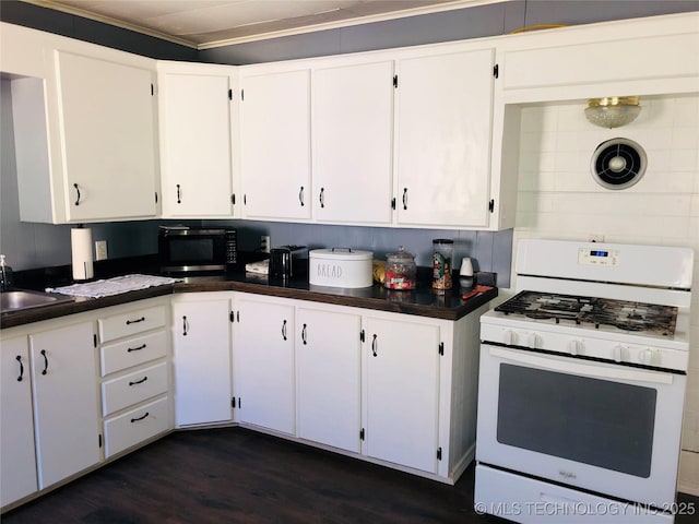 kitchen with dark wood-style floors, white gas stove, dark countertops, white cabinetry, and a sink