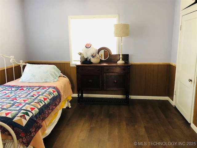 bedroom with wooden walls, dark wood-style flooring, and wainscoting