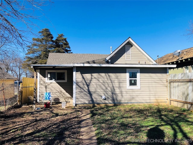 back of house featuring a shingled roof, fence, and a lawn