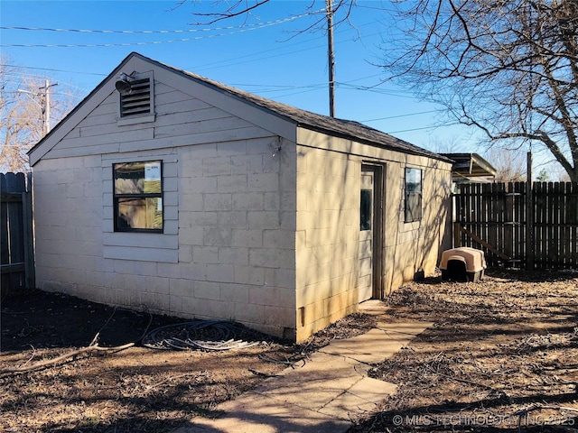 view of home's exterior with roof with shingles, concrete block siding, and fence