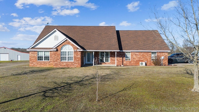 view of front facade featuring a shingled roof, a front yard, and brick siding