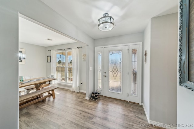 foyer with light wood finished floors, baseboards, and visible vents