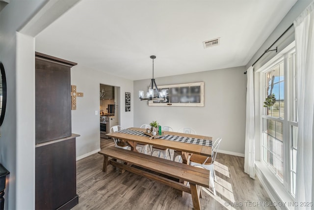 dining space with baseboards, light wood-type flooring, visible vents, and a notable chandelier