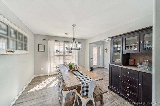 dining room with light wood finished floors, baseboards, visible vents, and a notable chandelier