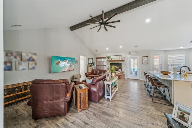 living room featuring light wood finished floors, visible vents, a ceiling fan, a brick fireplace, and beamed ceiling