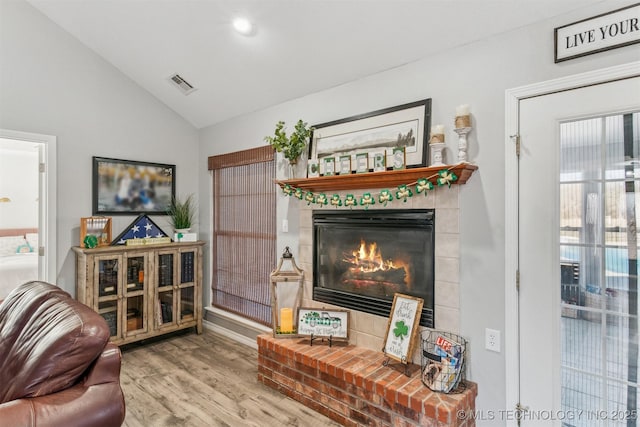 living area with lofted ceiling, a fireplace, visible vents, and wood finished floors