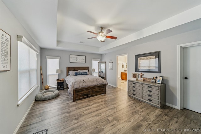 bedroom with multiple windows, baseboards, a raised ceiling, and wood finished floors