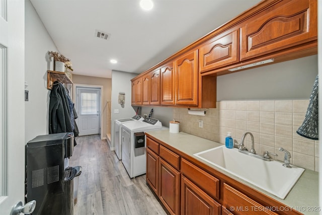 washroom with washer and clothes dryer, visible vents, cabinet space, light wood-style flooring, and a sink