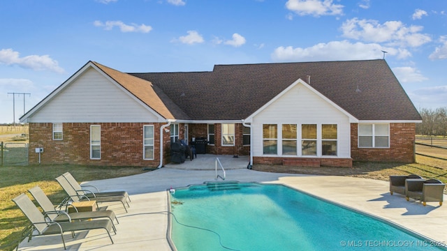 back of property featuring brick siding, roof with shingles, a fenced in pool, and a patio