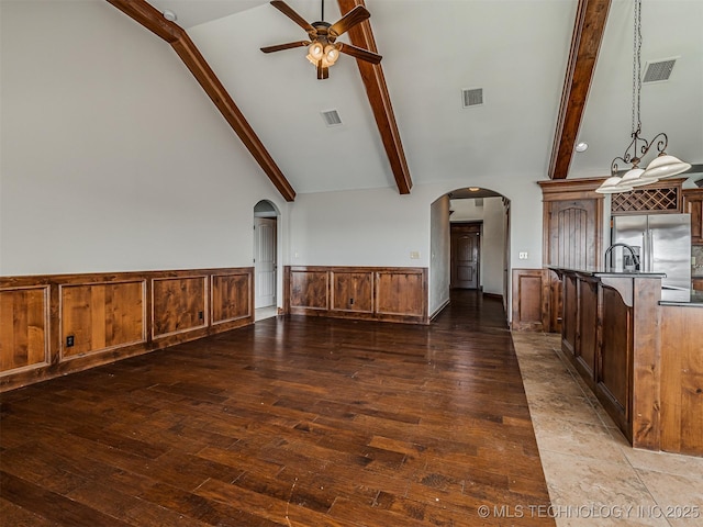 unfurnished living room with visible vents, arched walkways, beam ceiling, and wainscoting