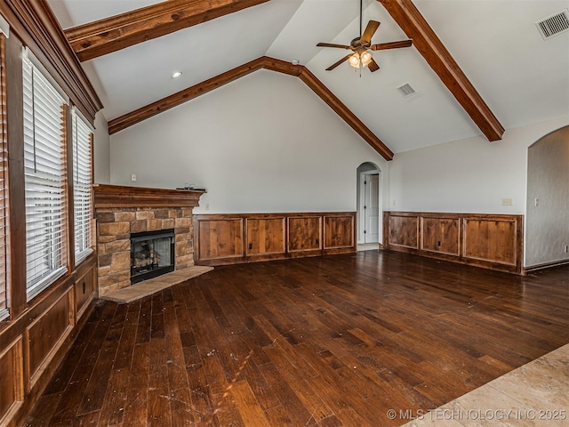 unfurnished living room featuring visible vents, beamed ceiling, hardwood / wood-style flooring, arched walkways, and a stone fireplace