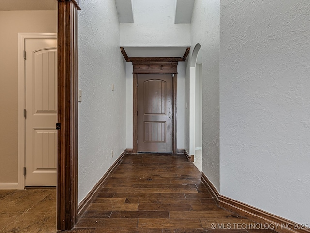 hall featuring arched walkways, baseboards, a textured wall, and wood finished floors