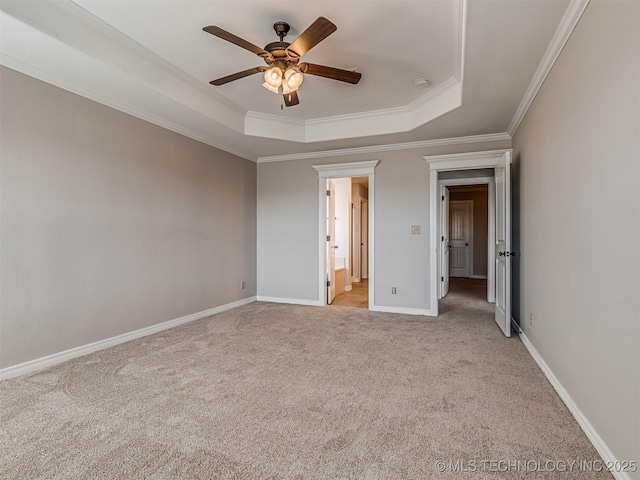 unfurnished bedroom with crown molding, baseboards, a tray ceiling, light carpet, and ensuite bath