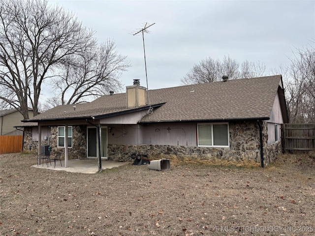 back of house featuring a patio, a chimney, stone siding, and fence