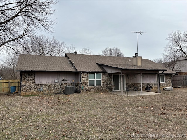 back of house featuring roof with shingles, a chimney, a patio area, fence, and stone siding