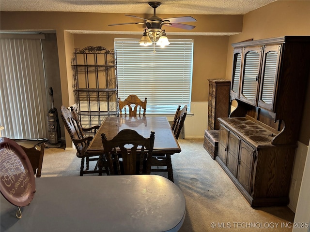 dining area with light carpet, a ceiling fan, a textured ceiling, and wainscoting