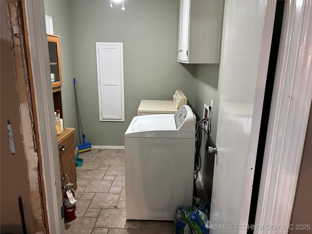 clothes washing area with cabinet space, stone tile floors, baseboards, and separate washer and dryer