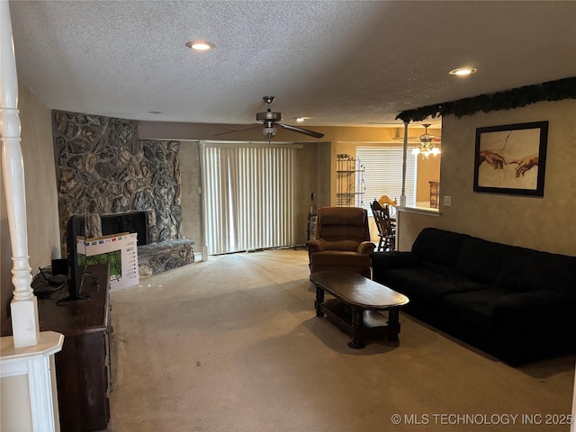 living area with a textured ceiling, carpet floors, a stone fireplace, and ceiling fan