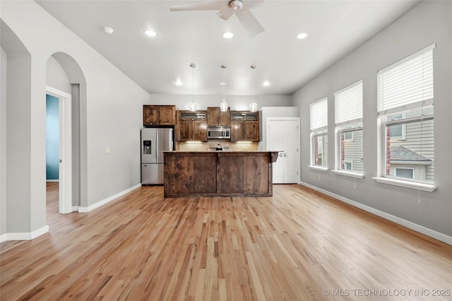 kitchen featuring arched walkways, appliances with stainless steel finishes, light wood finished floors, and baseboards