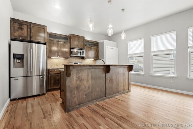 kitchen featuring light wood-style flooring, dark brown cabinetry, stainless steel appliances, baseboards, and decorative backsplash