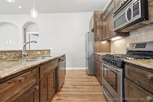 kitchen with light wood finished floors, decorative backsplash, light stone counters, stainless steel appliances, and a sink